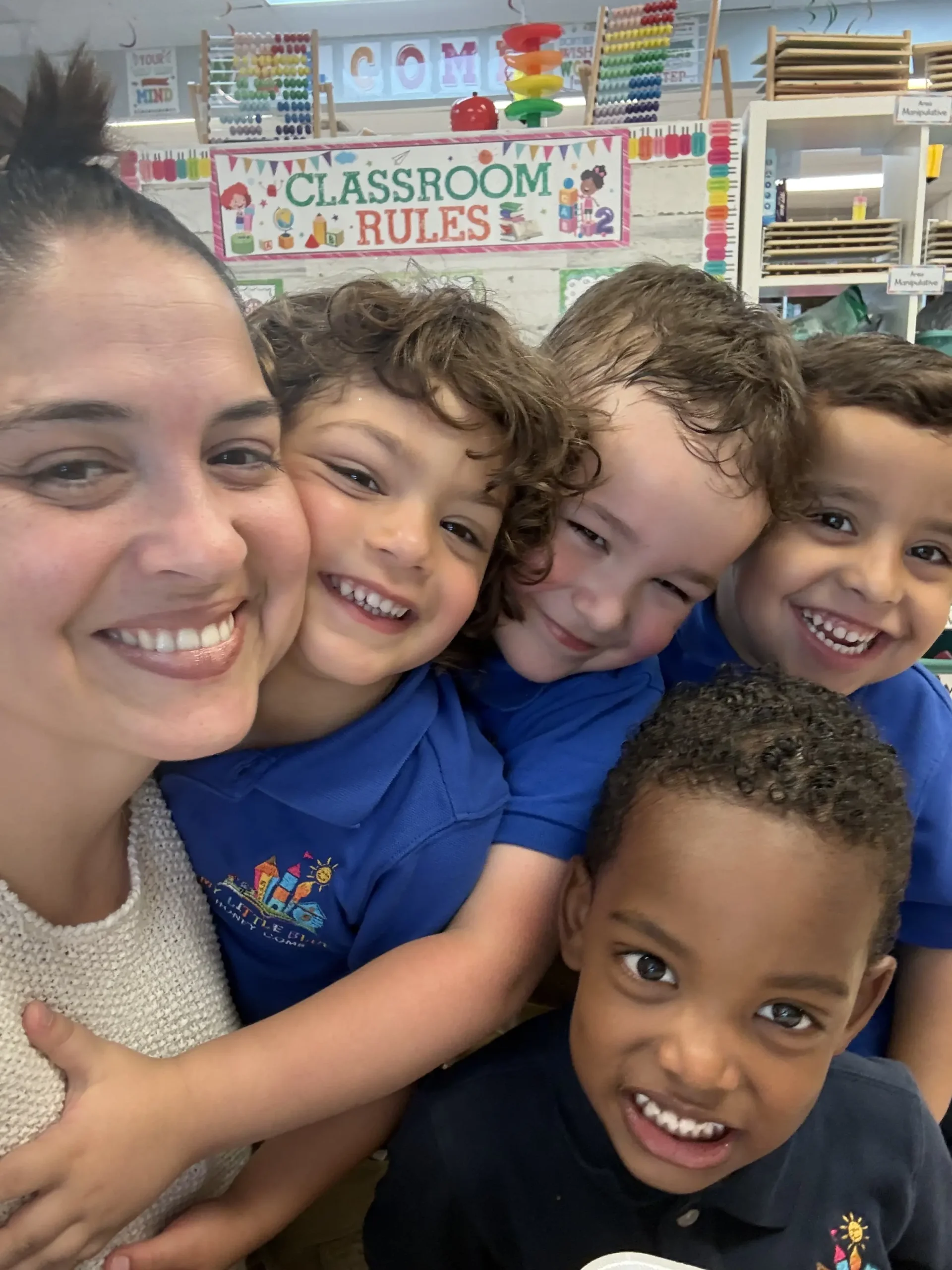 Happy preschool teacher hugging smiling students in a Miami Springs daycare classroom.