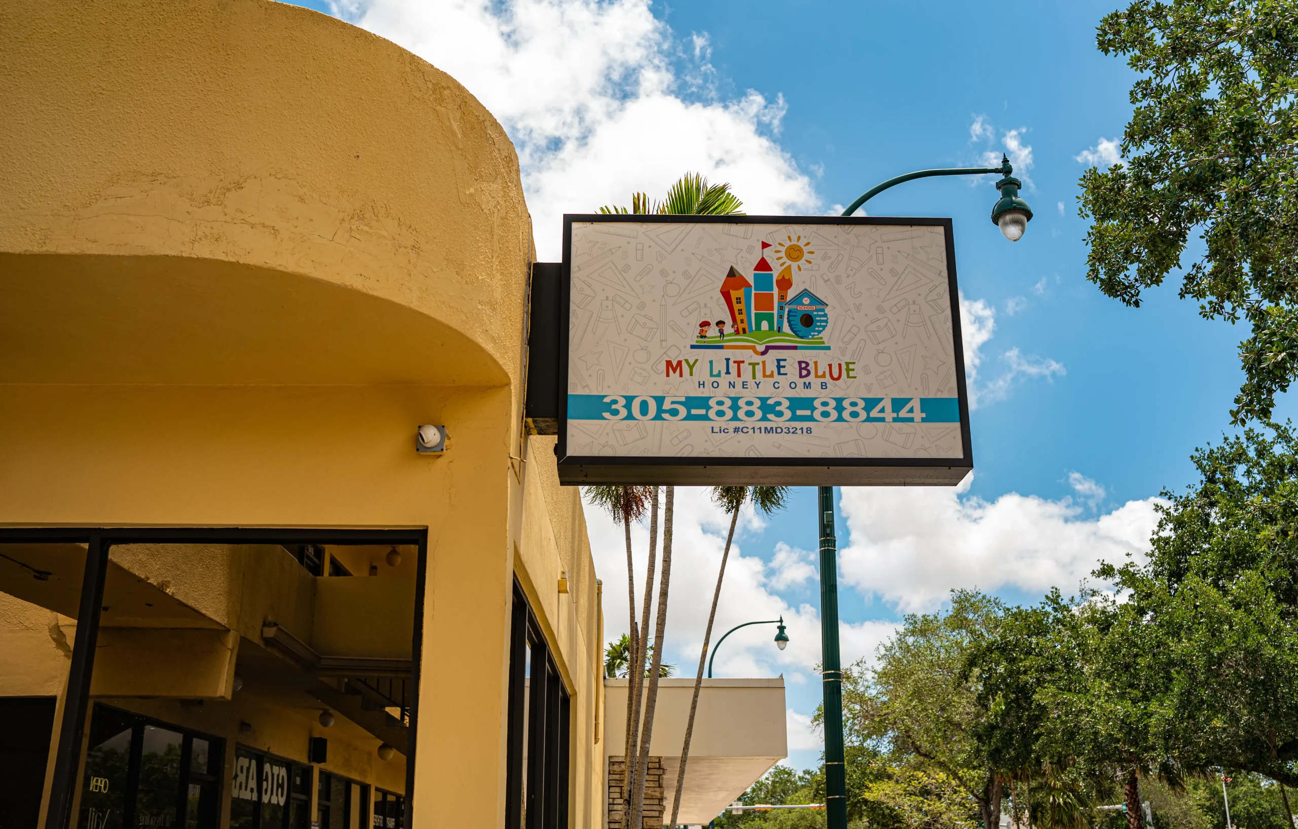 Outdoor storefront sign of My Little Blue Honeycomb childcare and early learning center in Miami Springs, showing the phone number 305-883-8844 and license number.