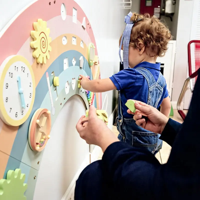 A toddler practicing fine motor skills and learning shapes with an interactive rainbow sensory board at My Little Blue Honeycomb childcare.